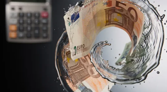 Billets d'euros partiellement dissous dans une spirale d'eau tourbillonnante, avec une calculatrice floue en arrière-plan